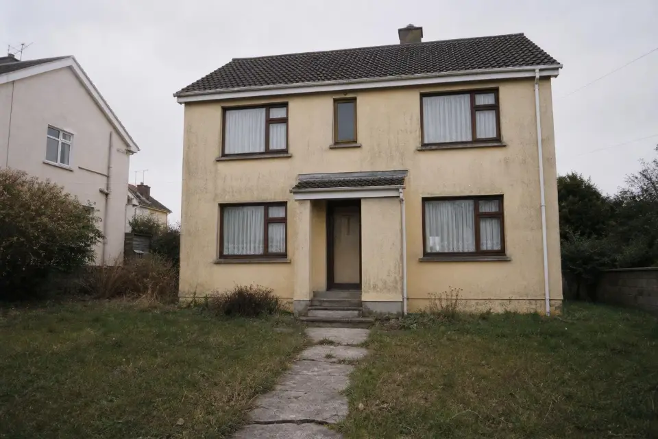 A tired 1970s detached house with a faded yellow rendered facade and a patchy lawn.